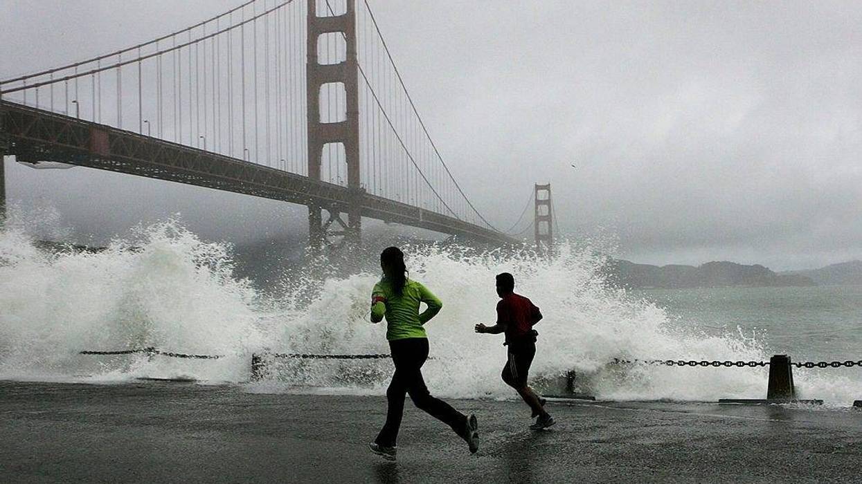 Two runners watch as a waves crash against the rocks at Fort Point near the Golden Gate Bridge December 28, 2005 in San Francisco.