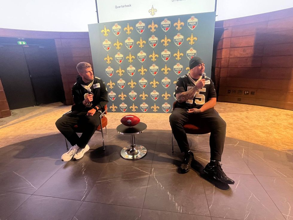 Two Saints football players speaking at an NFL Paris event, a football on a table.