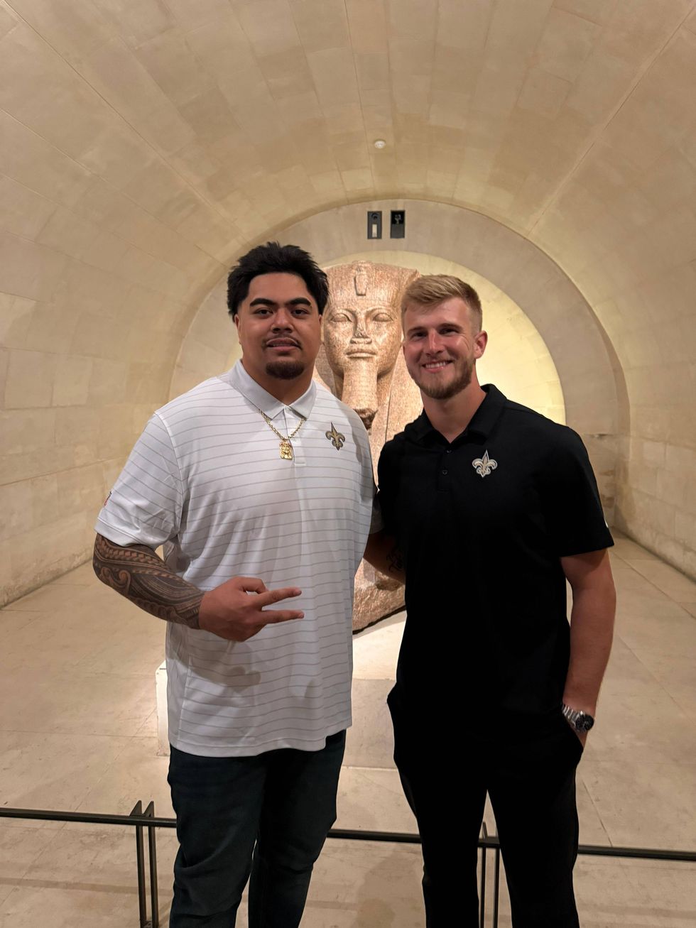 Two smiling men in New Orleans Saints polo shirts pose in front of an ancient Egyptian pharaoh statue.