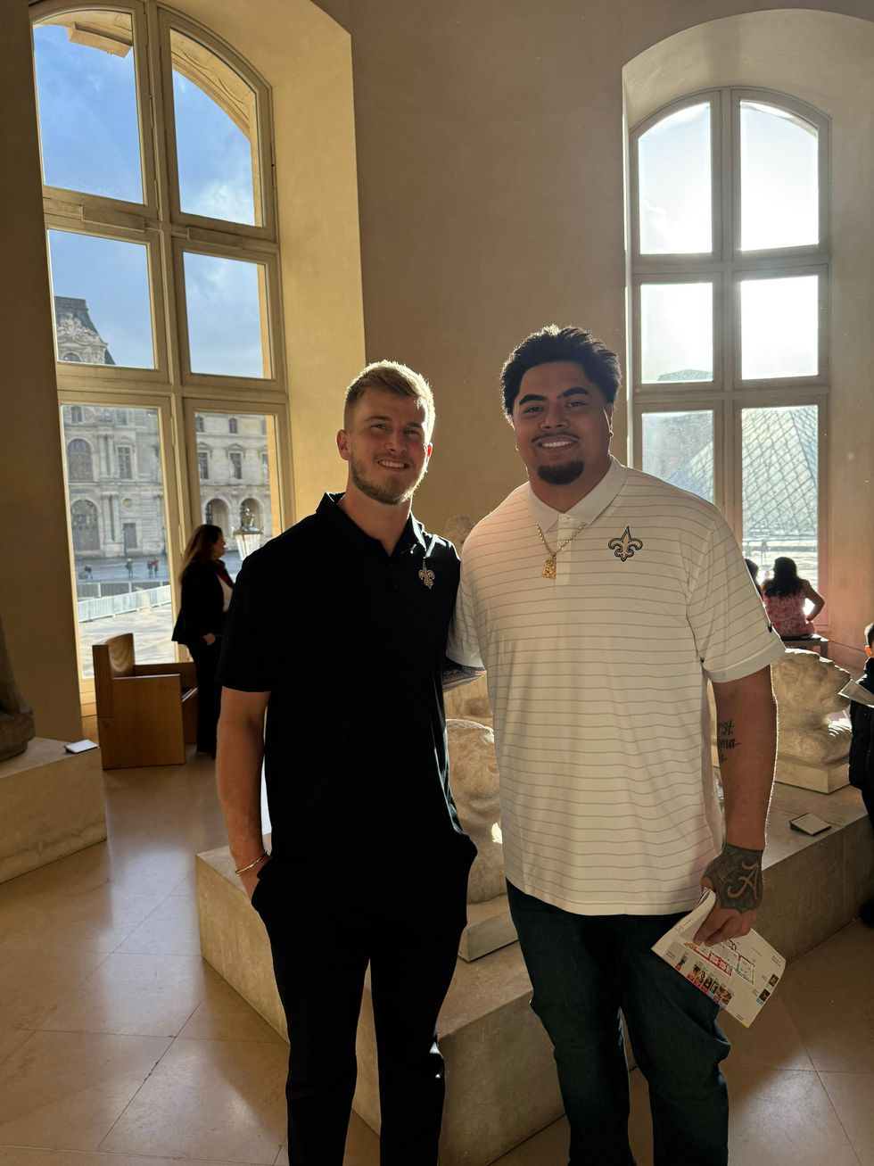 Two smiling men in New Orleans Saints polos inside the Louvre Museum.