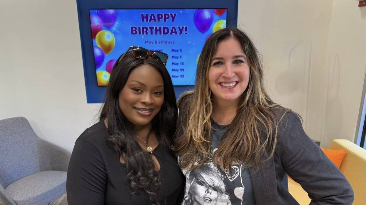 Two smiling women in front of a digital 'Happy Birthday!' display listing May dates.