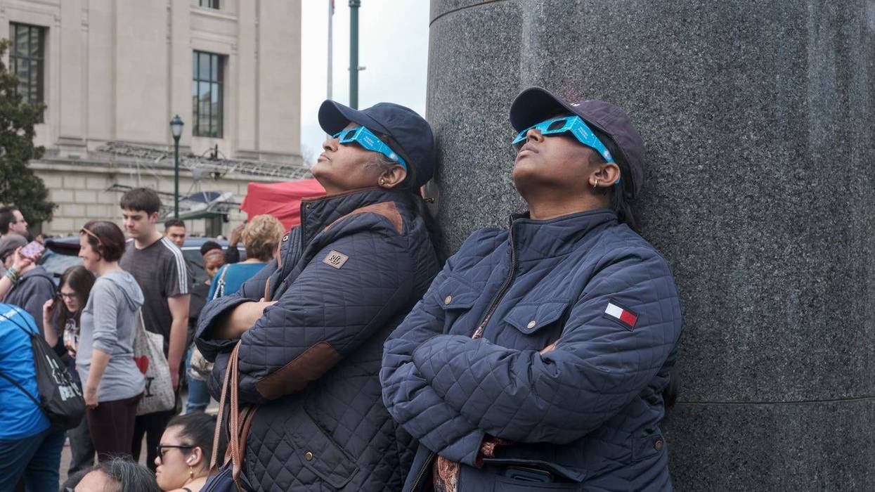Two women look up at the near total solar eclipse over Philadelphia on April 8, 2024.
