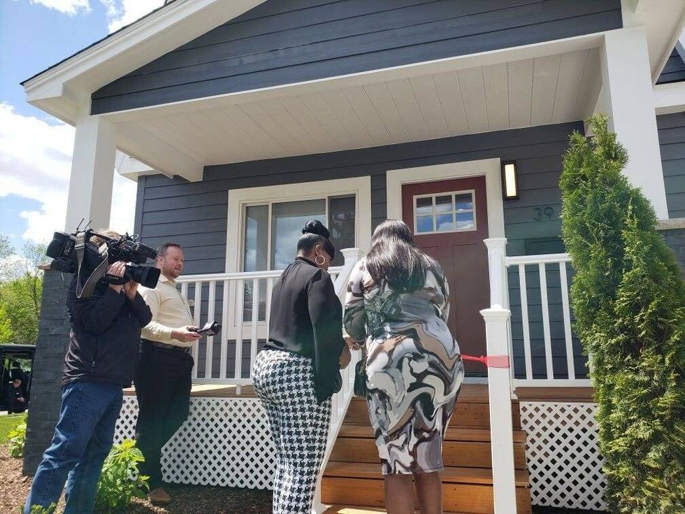 Two women walking into home, with camera man and reporter on side