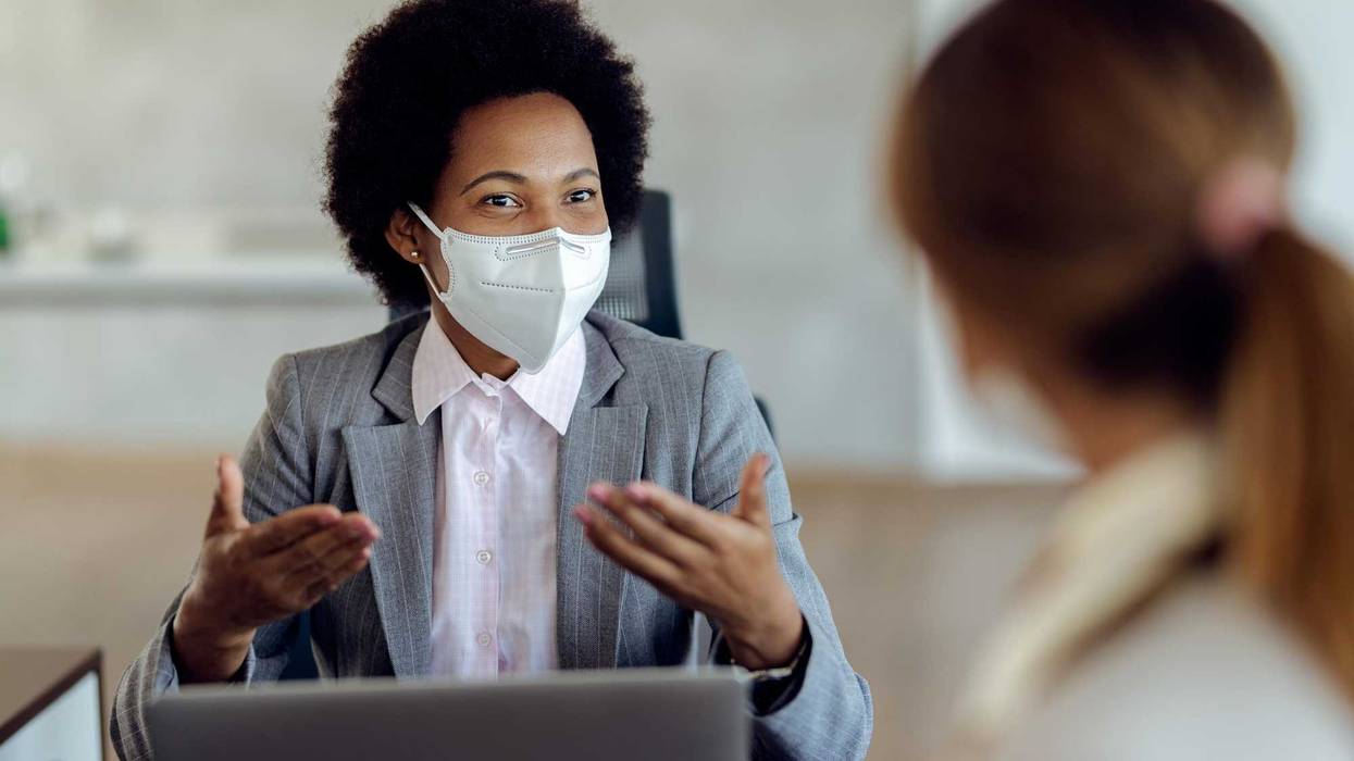 Two women with masks speaking to one another in a professional setting