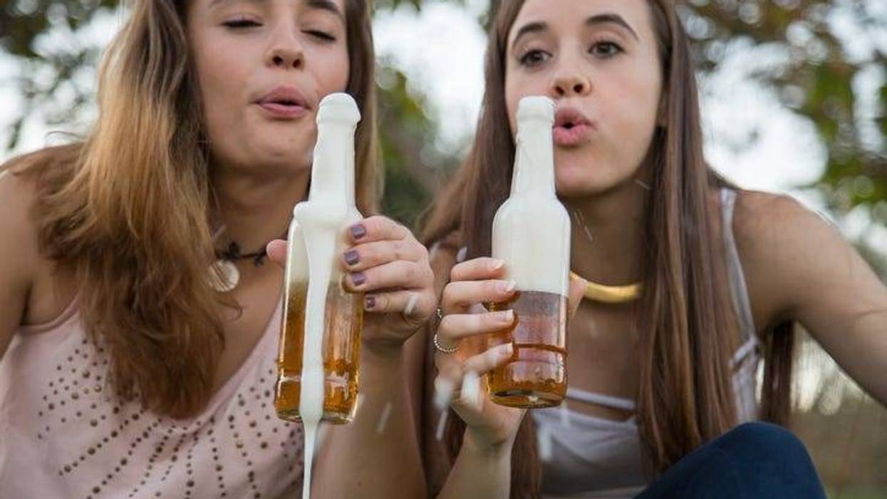 Two young laughing women celebrating with beer in park