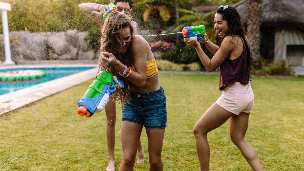 Two young people ambush another in a poolside water gun fight.