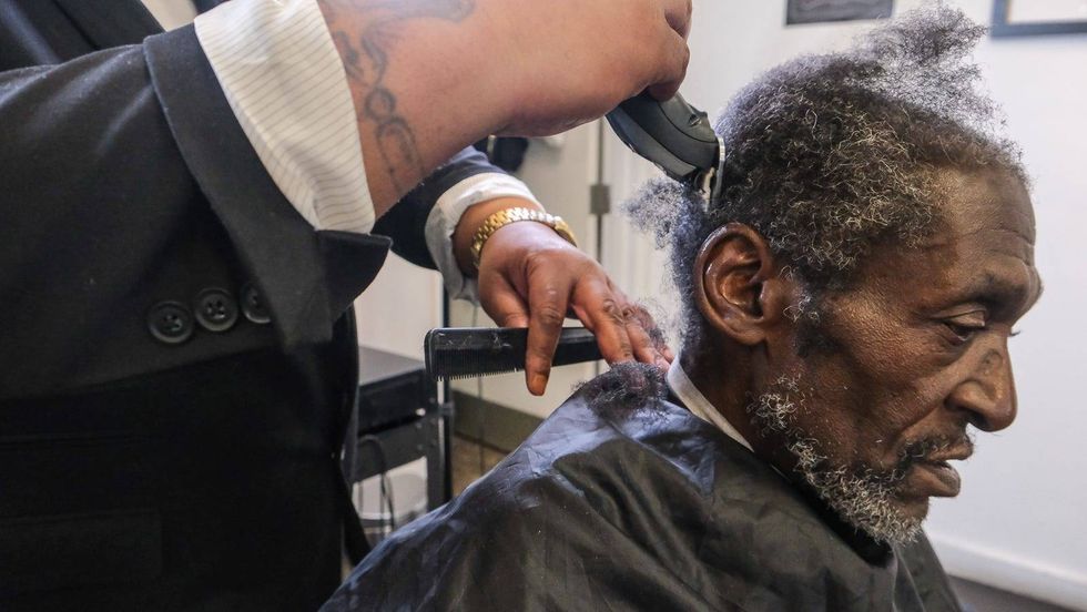 Tyce Combs works with client Yahya Muhammad, who has been coming to the school for more than 15 years to get his hair cut.