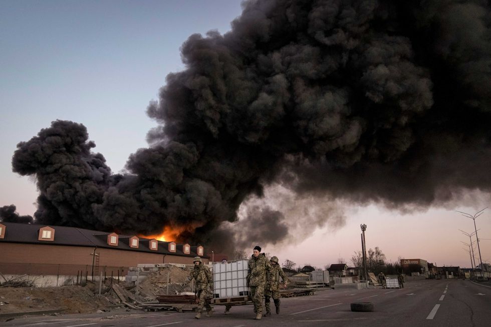 Ukrainian soldiers walk past a warehouse fire after a bombing on Thursday, March 17, 2022, on the outskirts of Kyiv