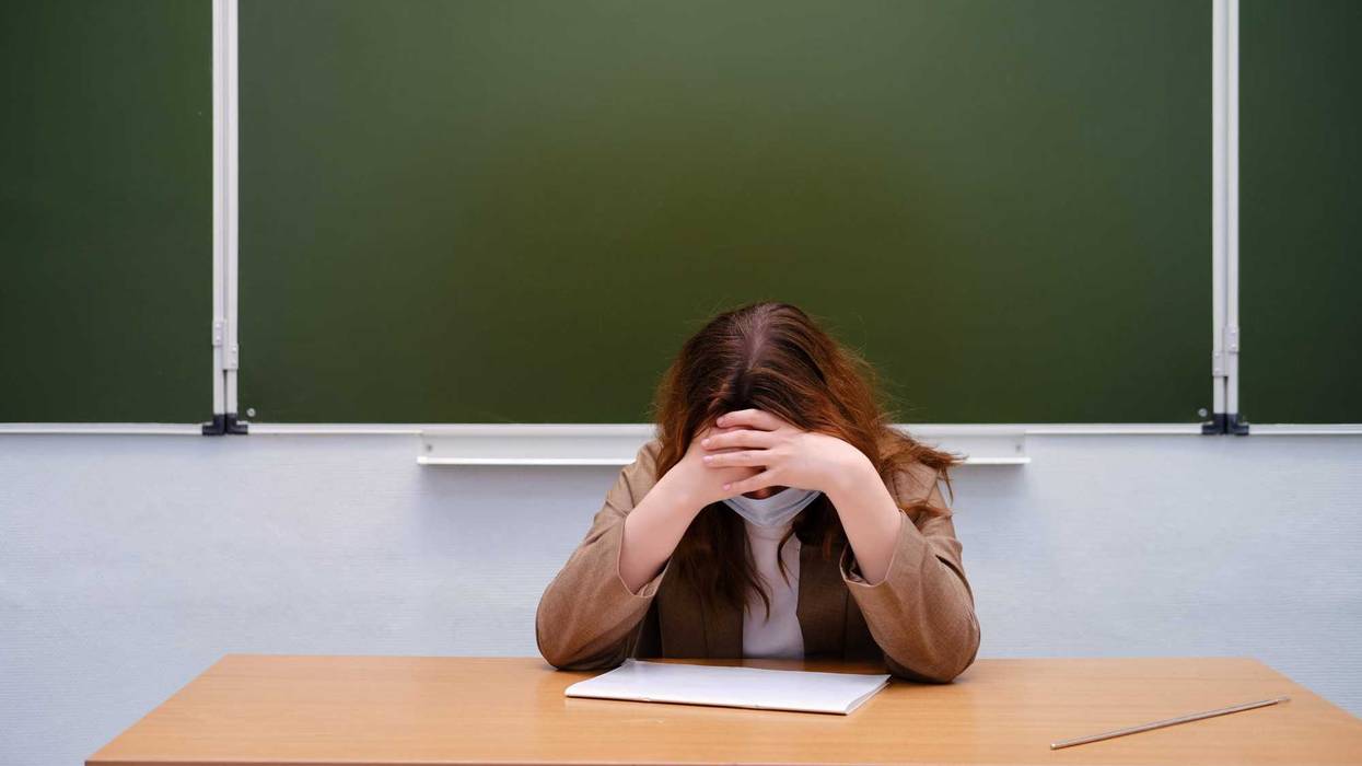 Upset teacher at desk in front of chalkboard.