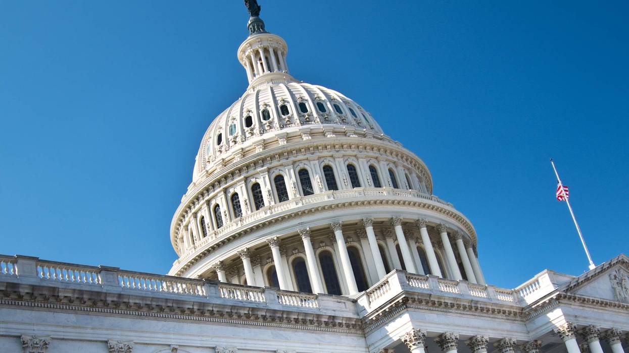 US Capitol Building dome and facade, US flag at half-mast against a clear blue sky.