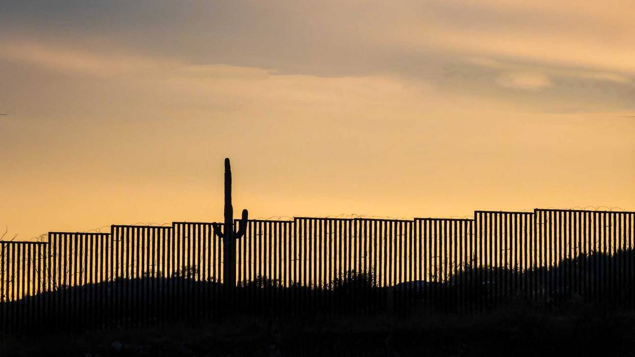 US -Mexico border wall at sunset with iconic saguaro cactus - stock photo