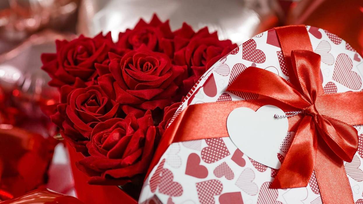 Valentine's day. Red roses in a white box in the form of a heart on the background of foil balls. A gift for women on a holiday. The concept of delivering flowers. floristry and flower shops. - stock photo