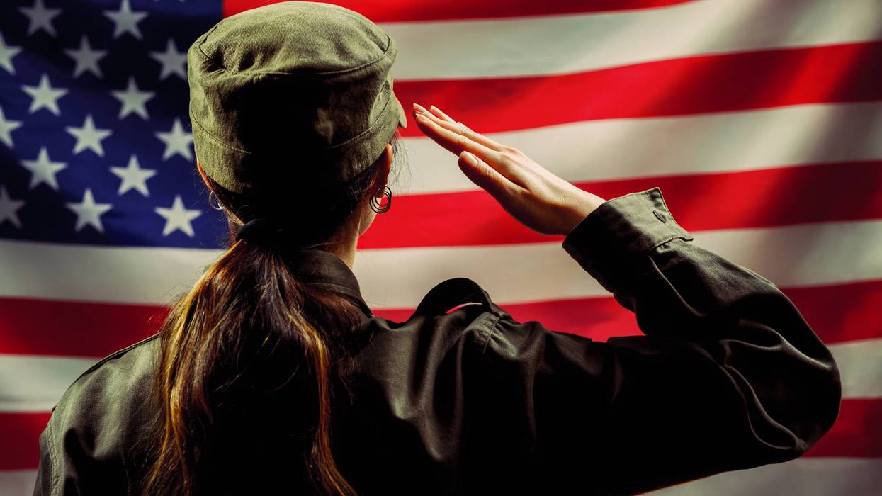 Veterans Day, Memorial Day, Independence Day. A female soldier salutes against the background of the American flag. Rear view. The concept of the American national holidays and patriotism