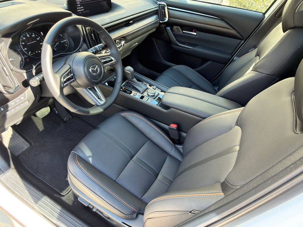 View of a Mazda car's modern black leather interior with orange stitching, steering wheel, and dashboard.