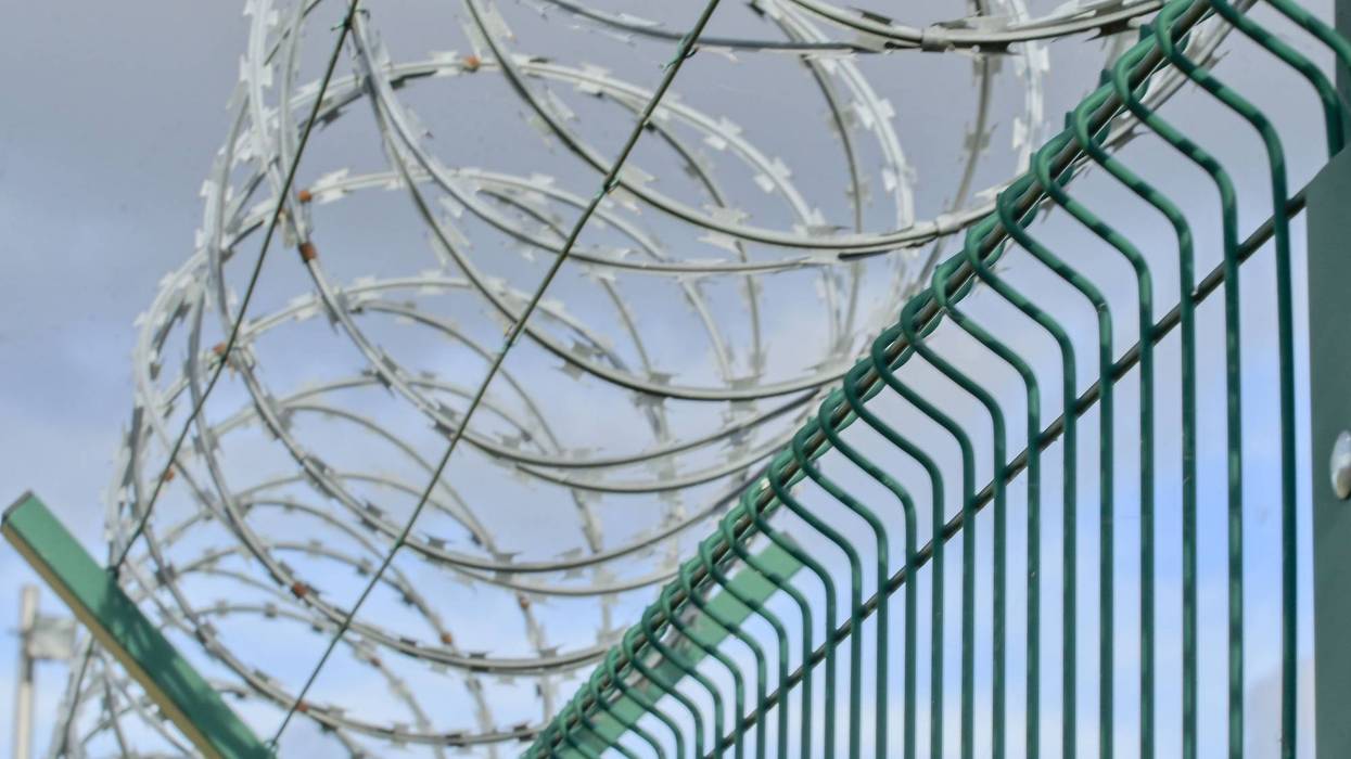 View of a prison fence topped with razor wire. Iron fence topped with barbed wire. Concept of guarded facilities, prisons, and military buildings.