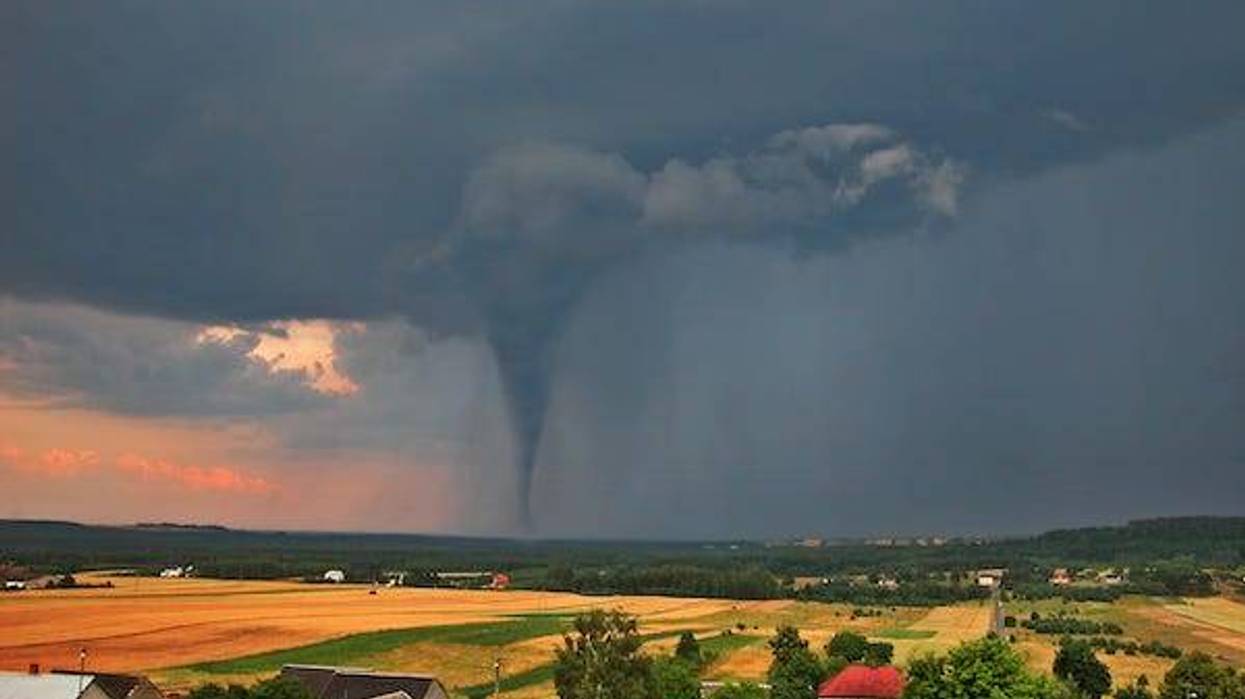 View of the serene countryside and stormy sky with a tornado in the background