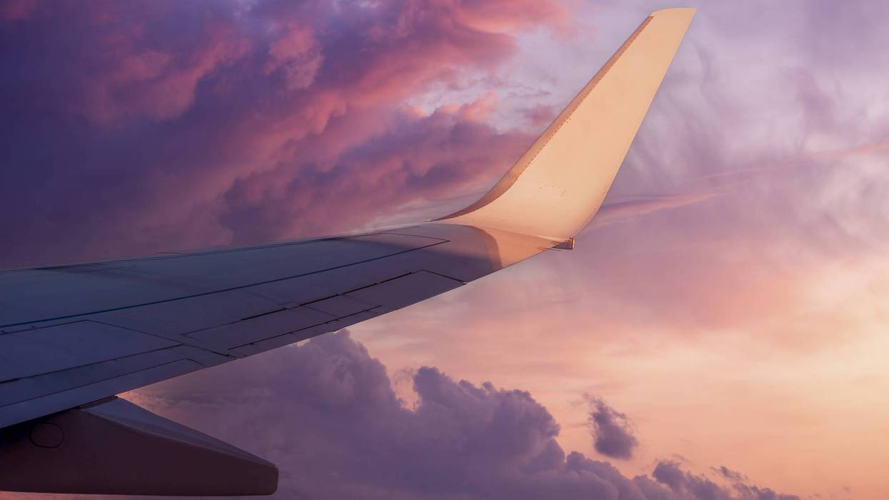 View of the wing of a flying airplane in the purple clouds of the setting sun