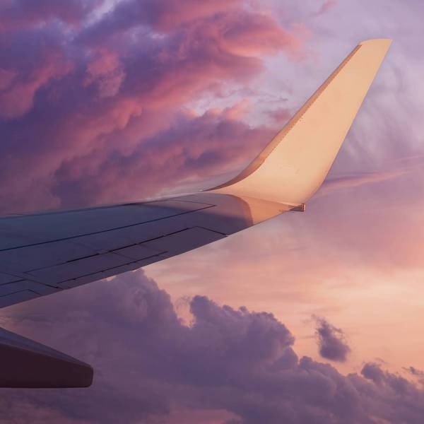 View of the wing of a flying airplane in the purple clouds of the setting sun