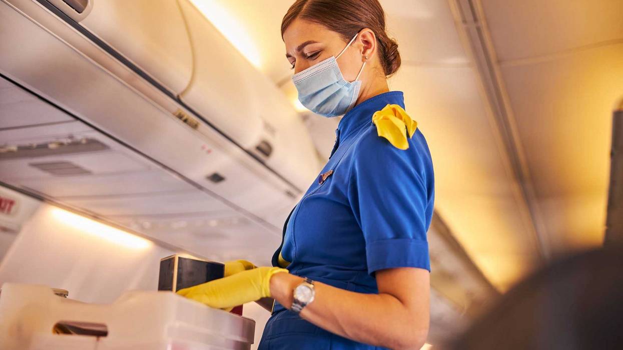 Waist-up photo of a flight attendant in a face mask and yellow gloves distributing meals to the passengers