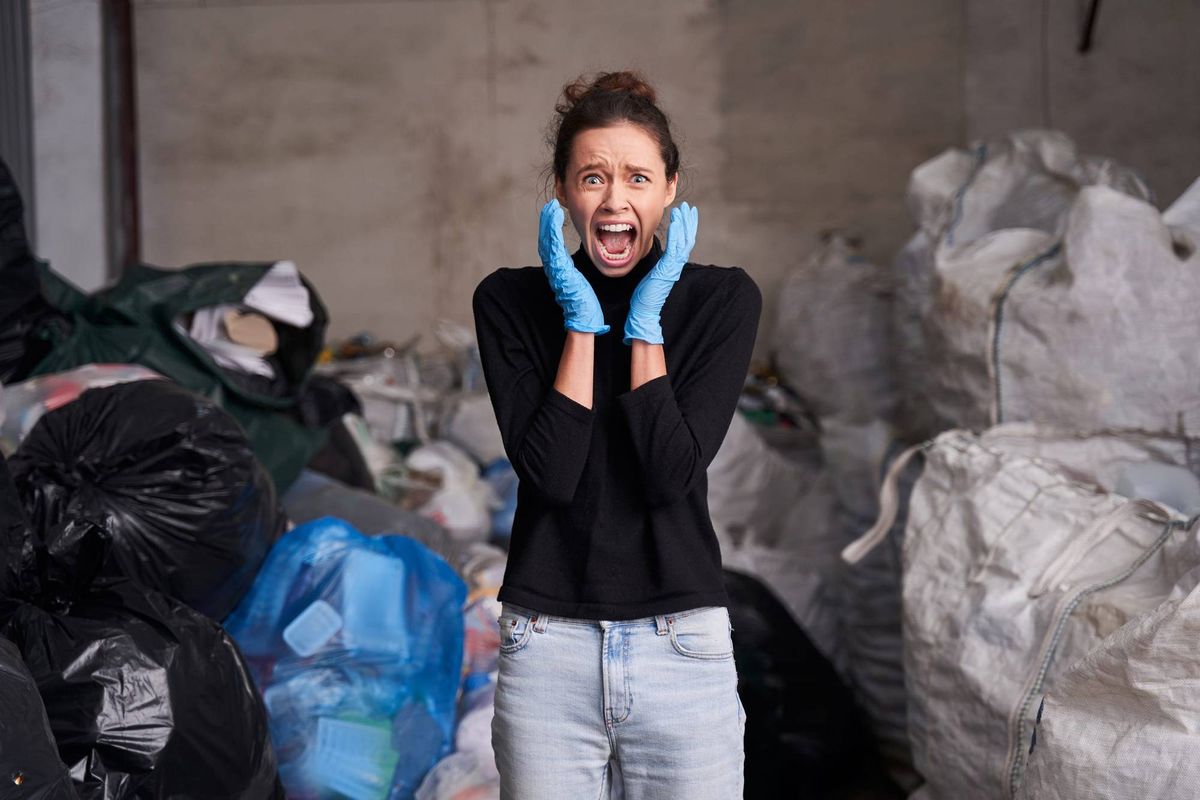 Waist up portrait of shocked caucasian woman screaming with hands near her face while working at the waste recycling plant
