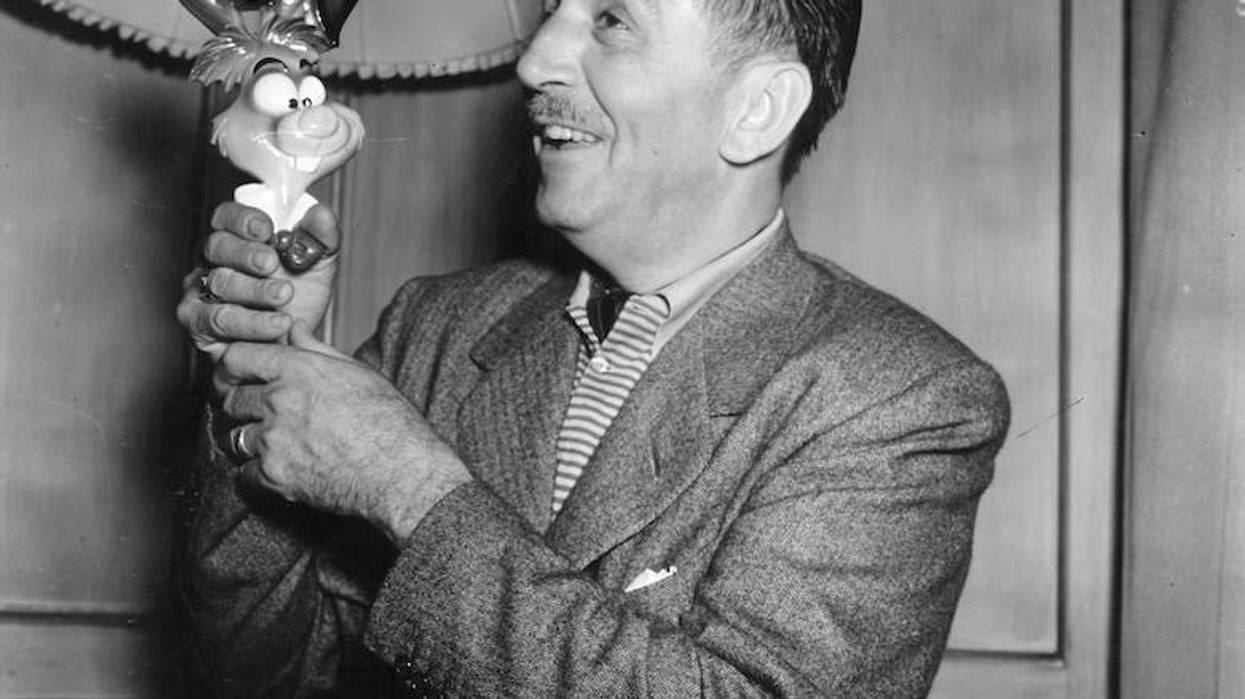 Walt Disney smiling, holding a White Rabbit toy from Alice in Wonderland. Black and white photo.