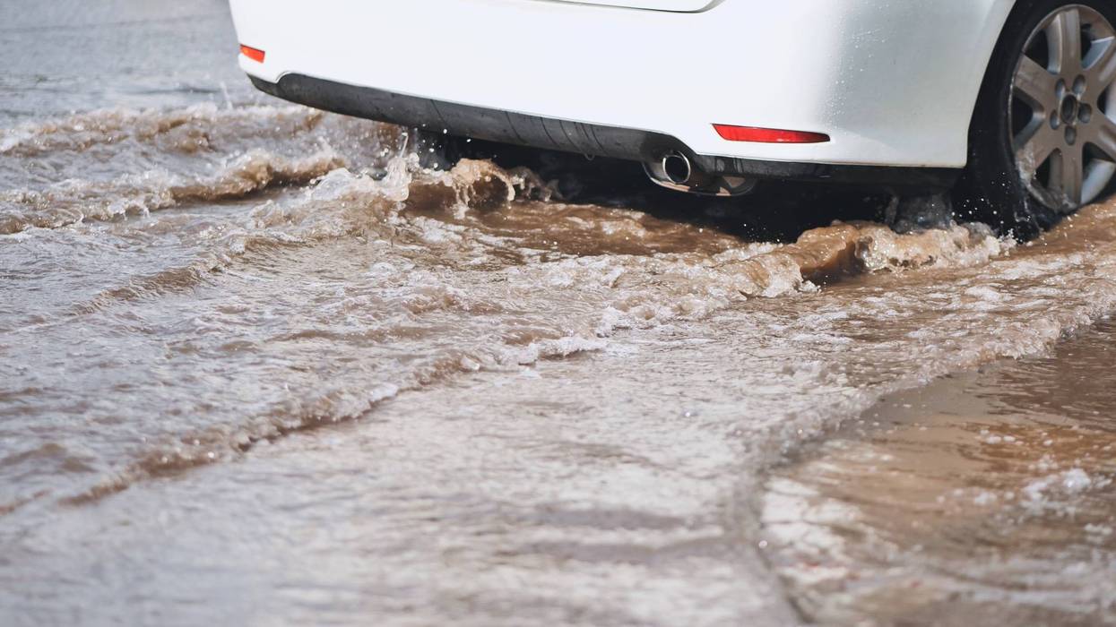 Water covered street showing vehicle plowing through flood, generating dramatic spray