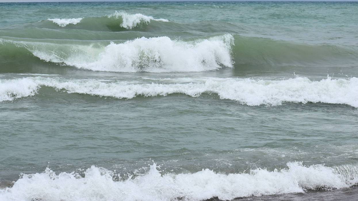 waves with white foam breaking and rolling onto a dark beach under a cloudy sky.