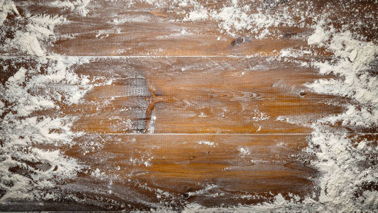 Wheat flour sprinkled on pastry board. Wooden background, top view, space for text.