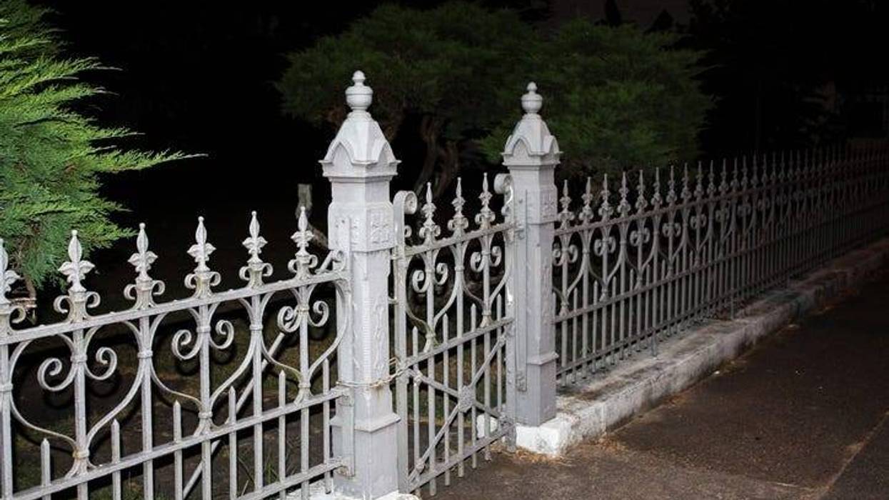 white stone or plaster fence with ornate wrought iron meeting at a creepy eerie cemetary gate with posts. taken in total darkness with one green tree on the side