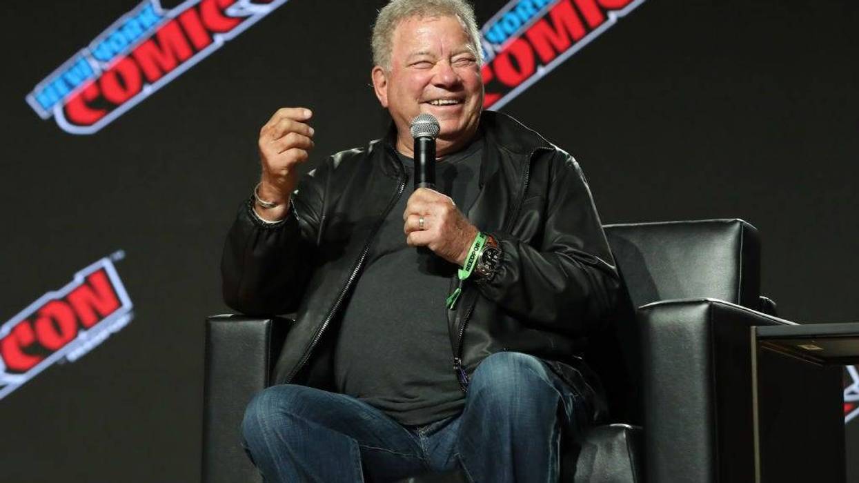 William Shatner sitting down and laughing with a microphone in his hand
