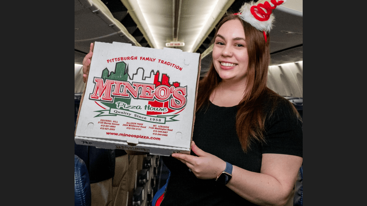 Woman holding a box of Mineo's pizza inside an airplane
