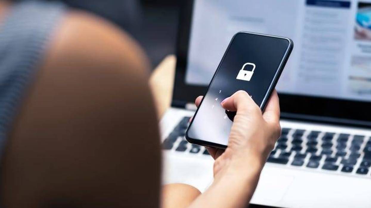 woman holding a cell phone while sitting in front of a laptop