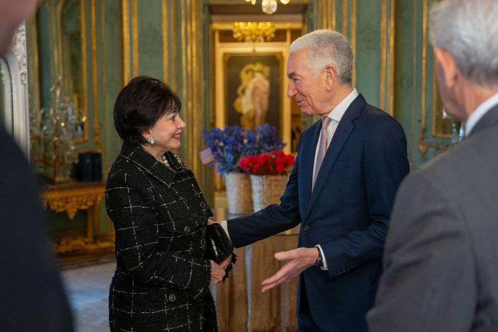 Woman in black jacket smiles at gesturing man in blue suit in an ornate room.
