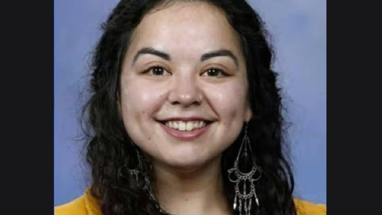 Woman in her 20s smiling with dark curly hair, wearing dangly earrings and yellow shirt