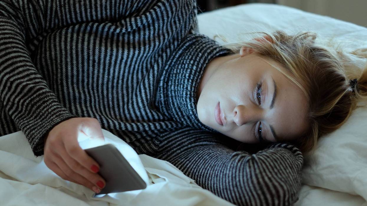 woman laying on bed looking at phone screen