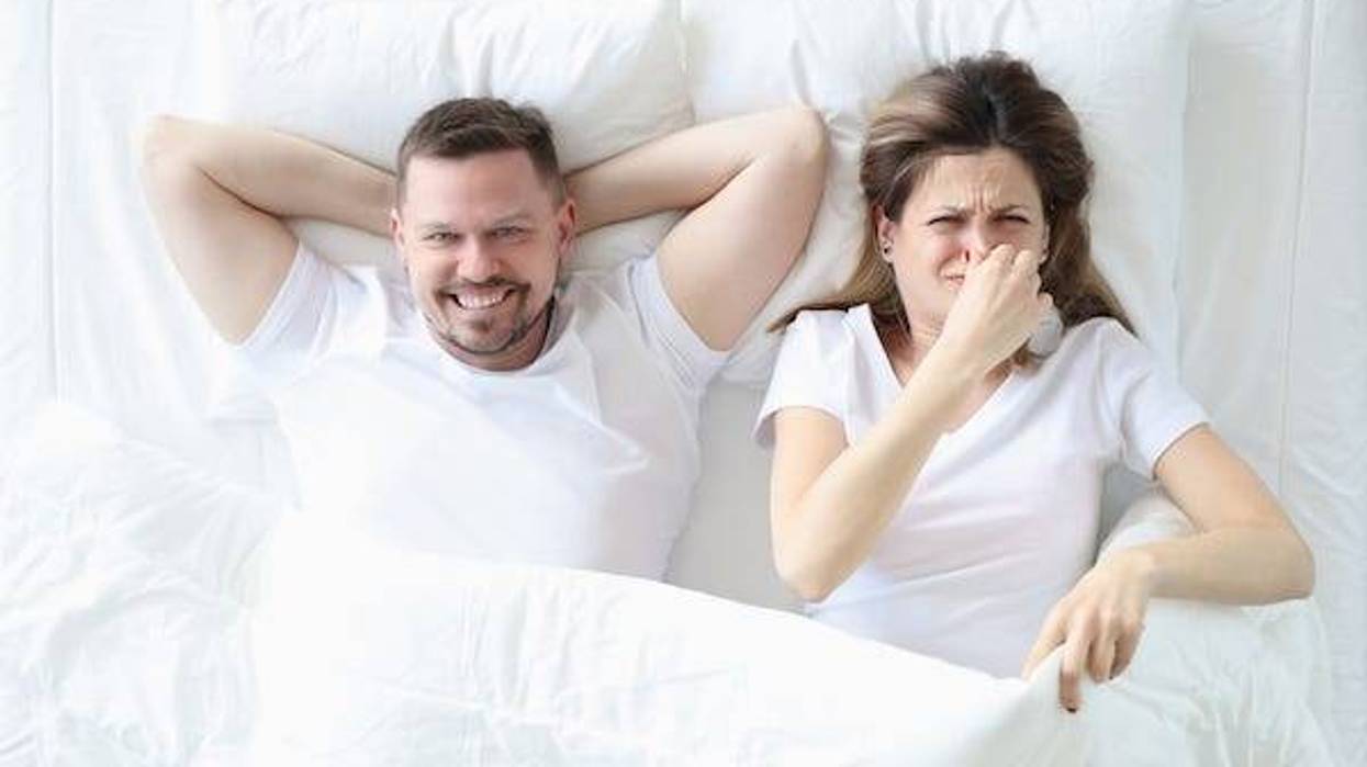 Woman lying in bed with man and covering her nose with her hand