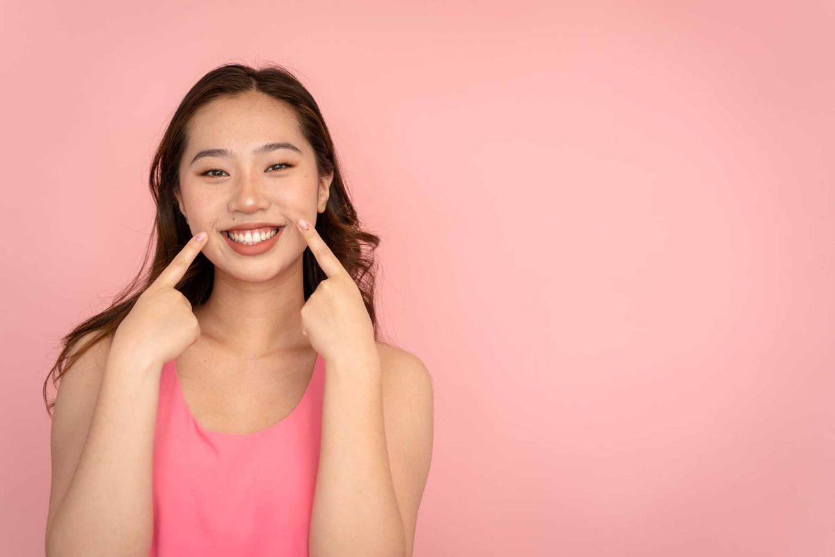 Woman smiling while pointing to her cheeks.