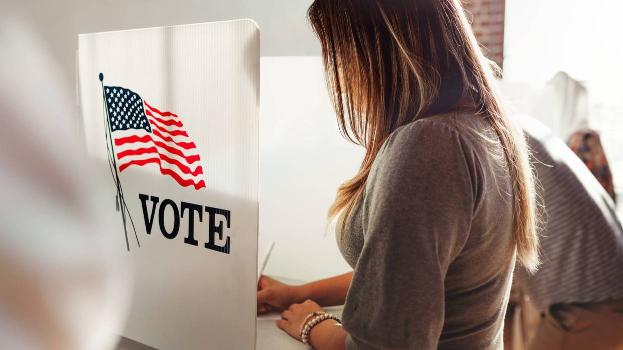 Woman stands in a voter booth, filling out a ballot