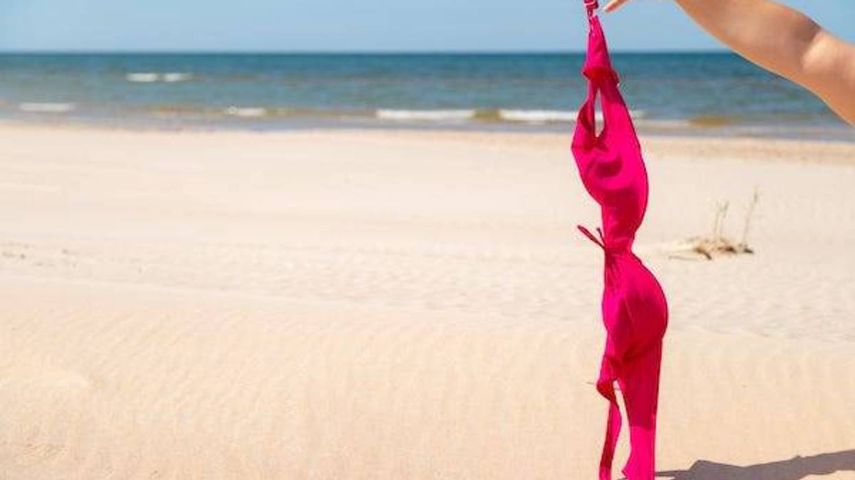 Woman taking off pink swimsuit top at the beach