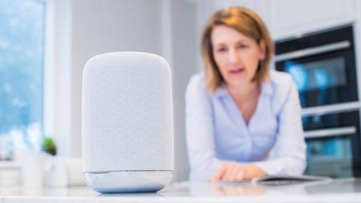 Woman talking to smart speaker device in kitchen