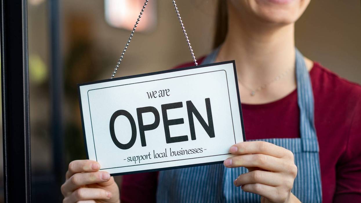 Woman turns sign to open welcoming customers back to the shop.