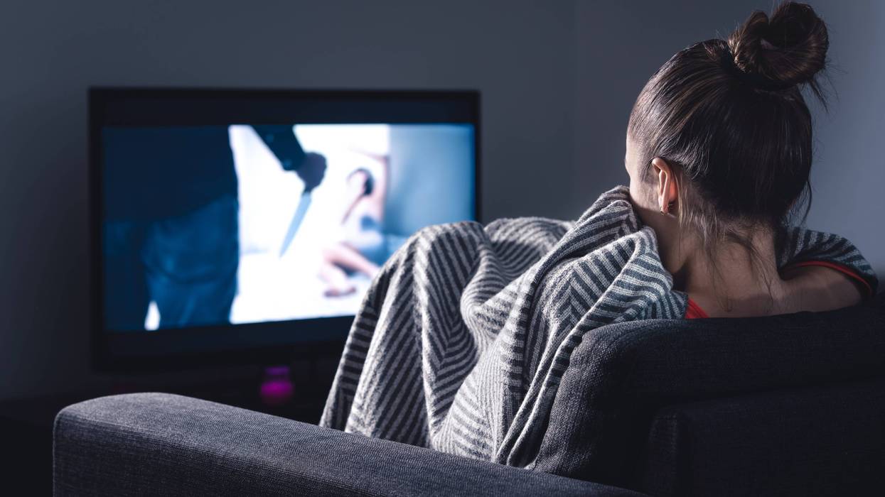 woman watching scary movie with blankets pulled up to her face