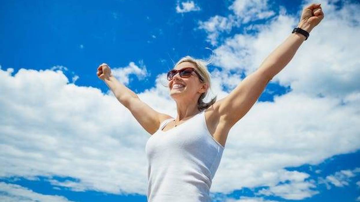 Woman with arms raised in the air against blue sky