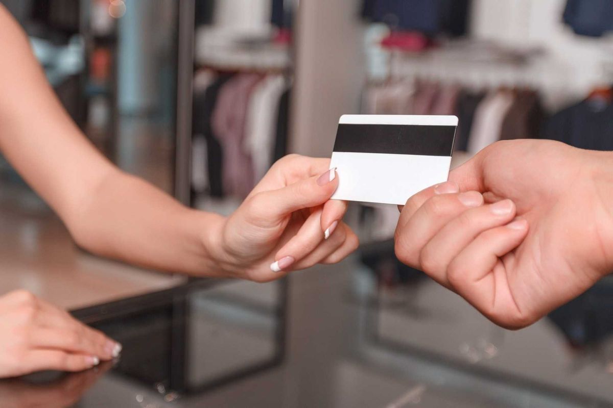 Woman with French manicure handing card back to man at a store.