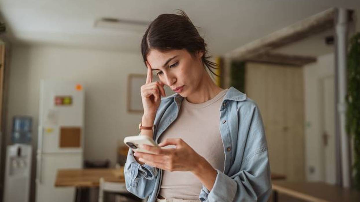 Woman with hand on forehead intently looking at her smartphone indoors, appearing thoughtful.