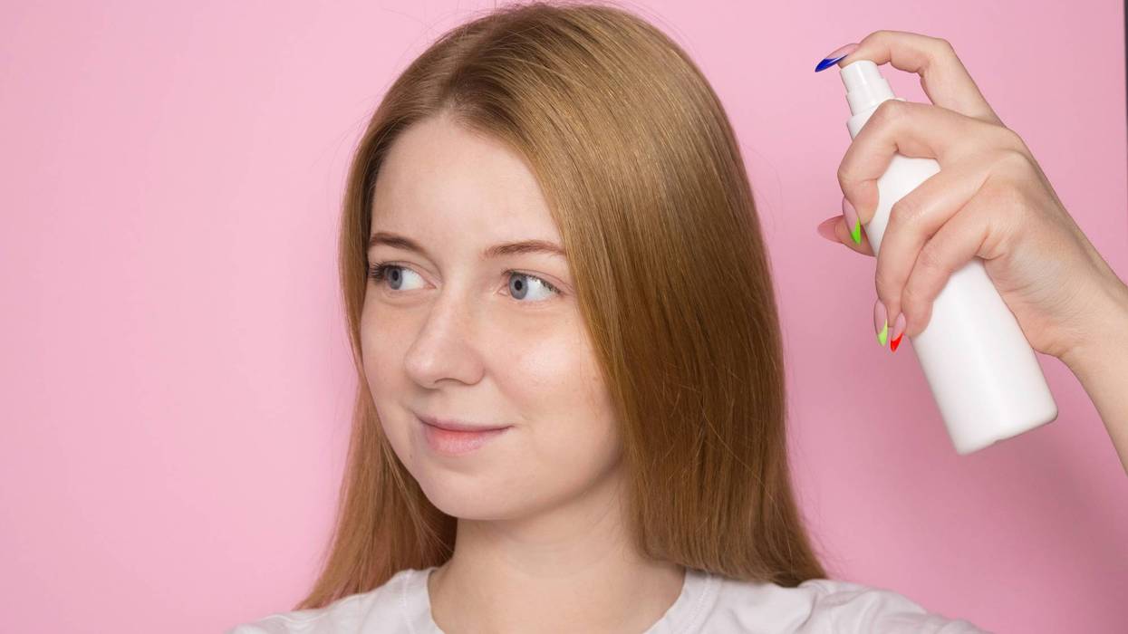 Woman with long hair holds a spray bottle in a white bottle and sprays it on her hair. Hair care product, body care.
