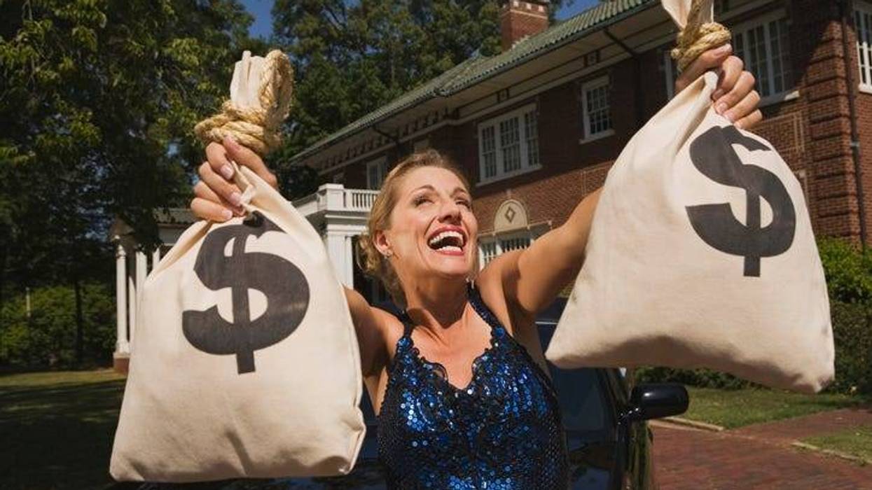 Woman with money bags in front of mansion - stock photo