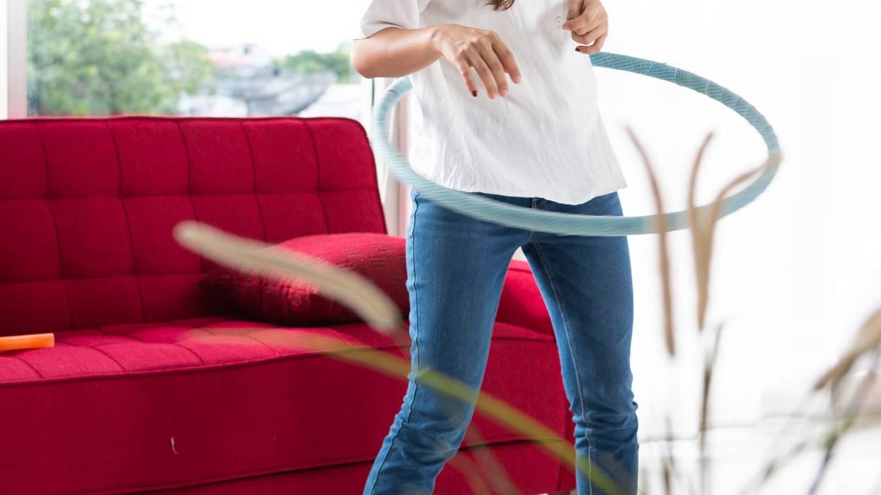 women playing Hula Hoop in the living room at home. Young adult woman learning to play with a hula-hoop in a living room.