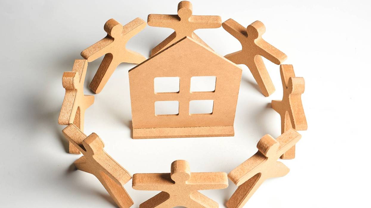 Wooden figures forming a protective circle around a house, symbolizing neighborhood support, safe housing and community care.