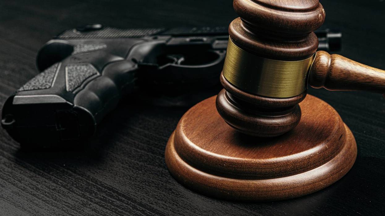 Wooden gavel and black handgun on dark wood, symbolizing gun laws.